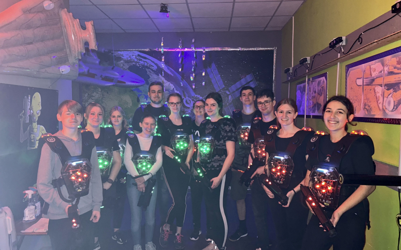 Auszubildende in leuchtenden Lasertag-Westen mit Spielger&auml;ten beim Gruppenfoto in der Lasertag-Halle