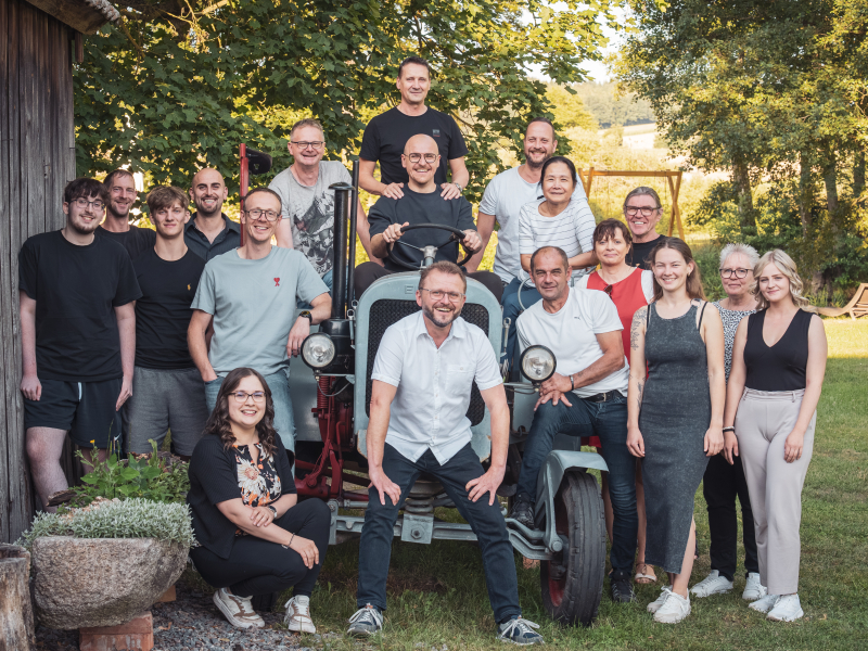 Gruppenfoto eines Teams um einen alten Traktor neben einer Holzscheune