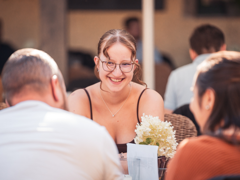 Eine junge Kollegin lacht im Gespr&auml;ch am Tisch