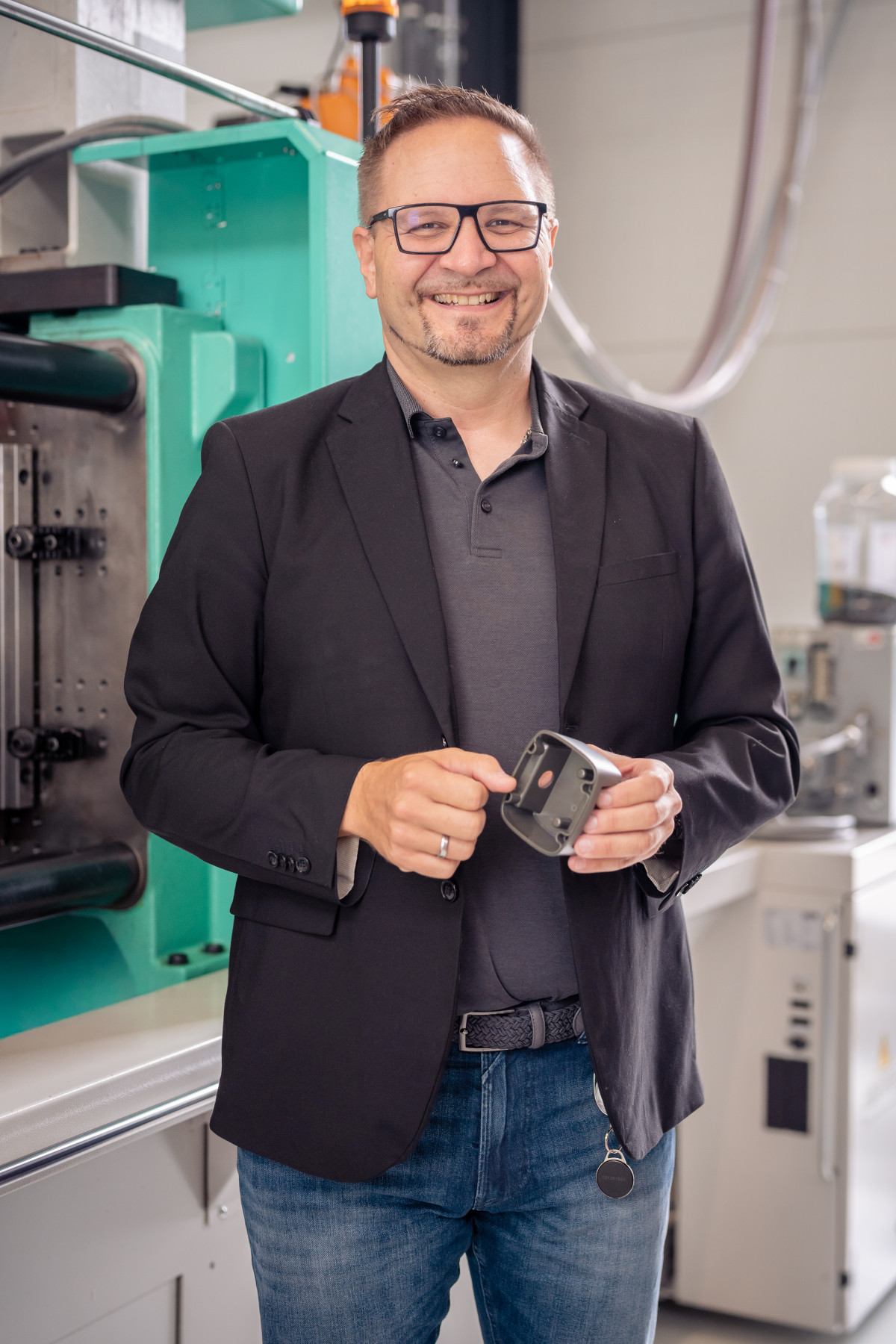 Porträt von Martin Reiß mit einem Kunststoffteil in der Hand vor einer Spritzgussmaschine
