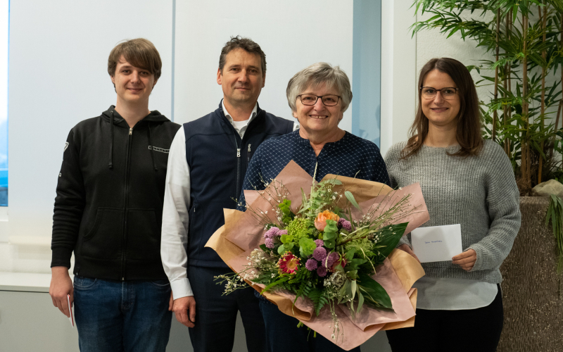 Vier Personen beim Firmenjubil&auml;um, eine Jubilarin h&auml;lt einen Blumenstrau&szlig;