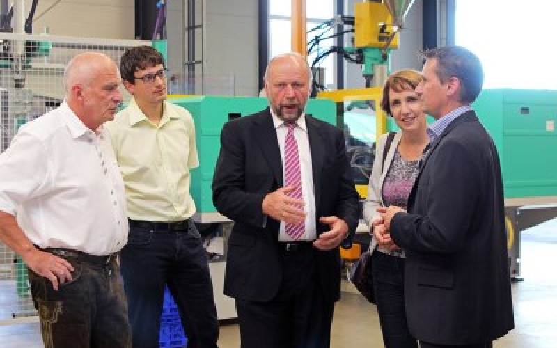 F&uuml;nf Personen im Gespr&auml;ch in der Produktionshalle, im Hintergrund Spritzgussmaschinen