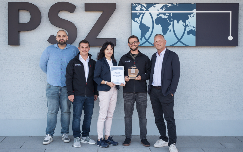 F&uuml;nf Mitarbeitende mit Urkunde und Glaspokal &bdquo;Supplier of the Year&ldquo; vor dem PSZ-Logo an der Fassade