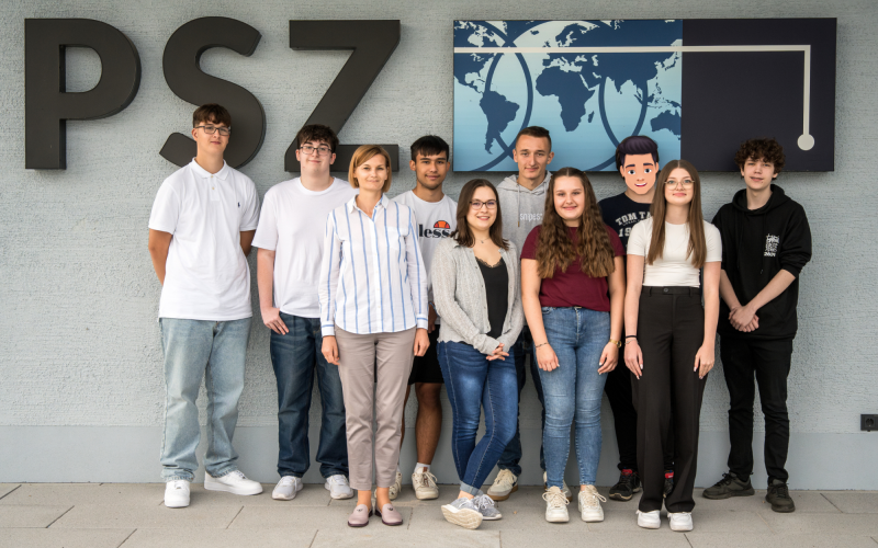 Gruppenfoto der neuen Auszubildenden 2024 mit einer Kollegin vor dem PSZ-Schriftzug an der Fassade