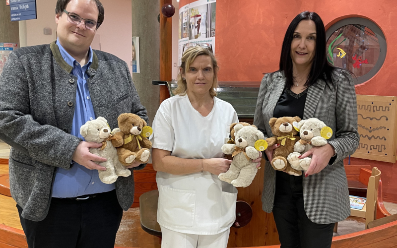 Drei Personen mit Pl&uuml;schteddys im Eingangsbereich eines Krankenhauses